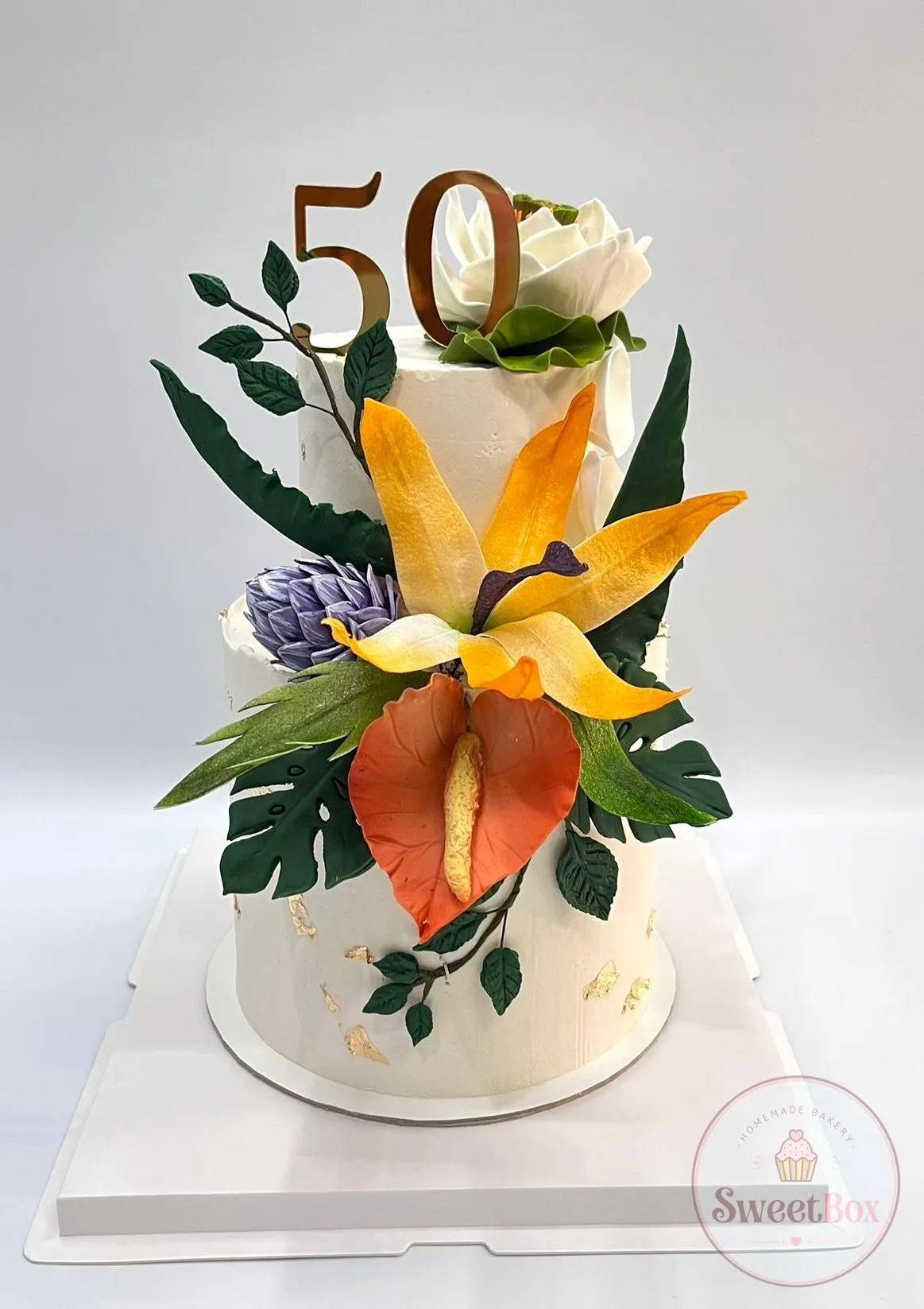 Two-tier 50th birthday cake with sugar bird of paradise flowers, leaves and a gold number 50 topper