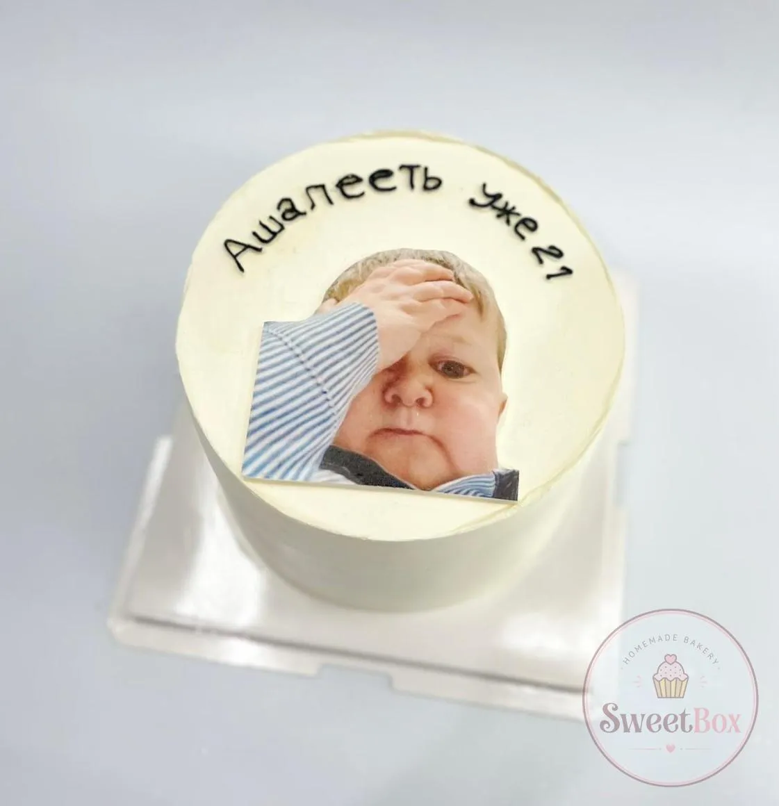 White bento cake with an edible print of a baby face-palming and a funny Russian caption