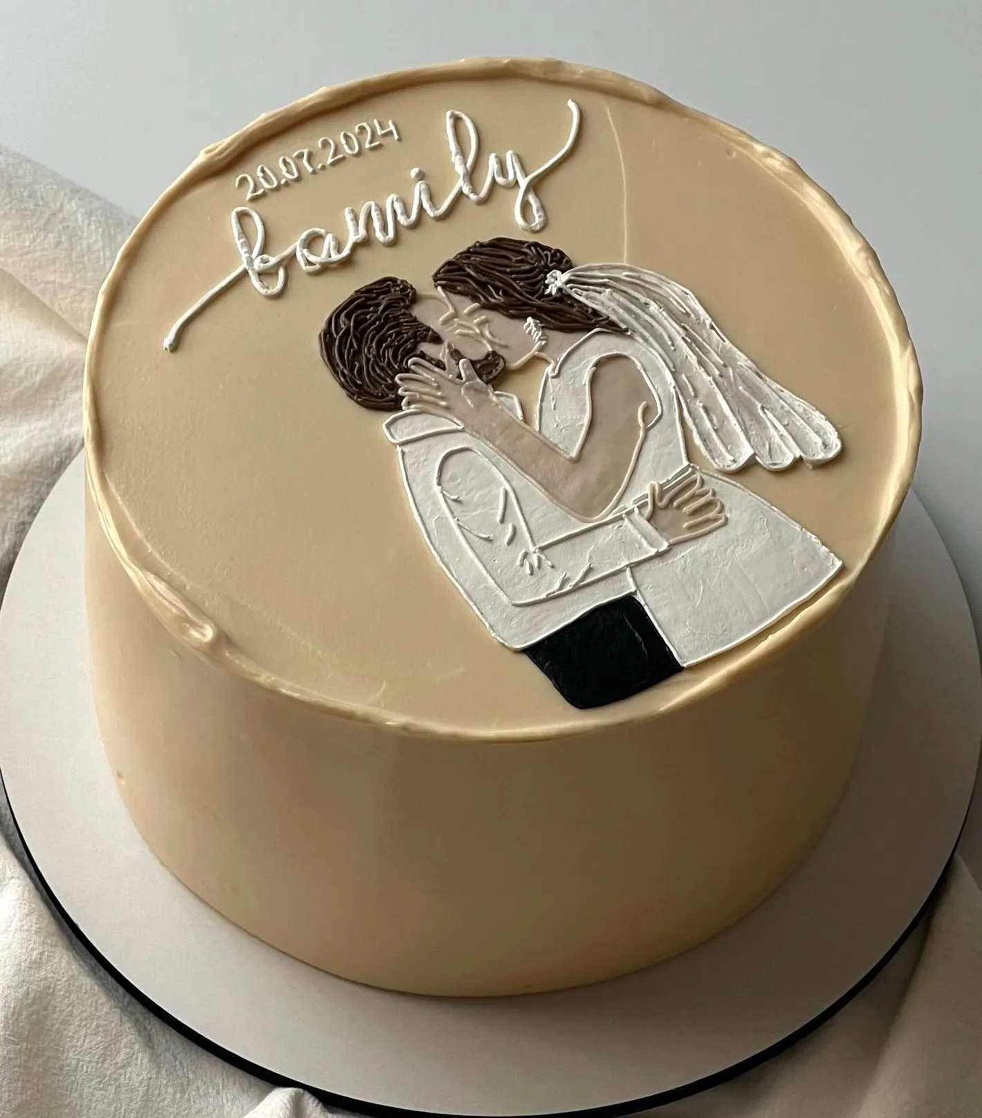 Beige cake with a hand-piped kissing bride and groom, family lettering and a date