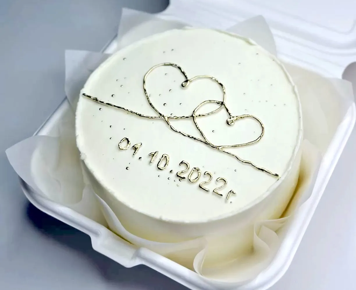 White bento cake in a lunch box with gold intertwined hearts and a date