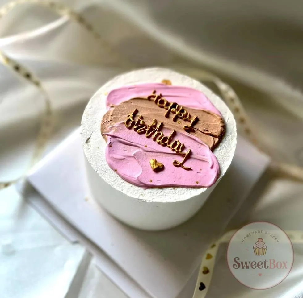 White bento cake with pink and brown brushstrokes and gold Happy Birthday script