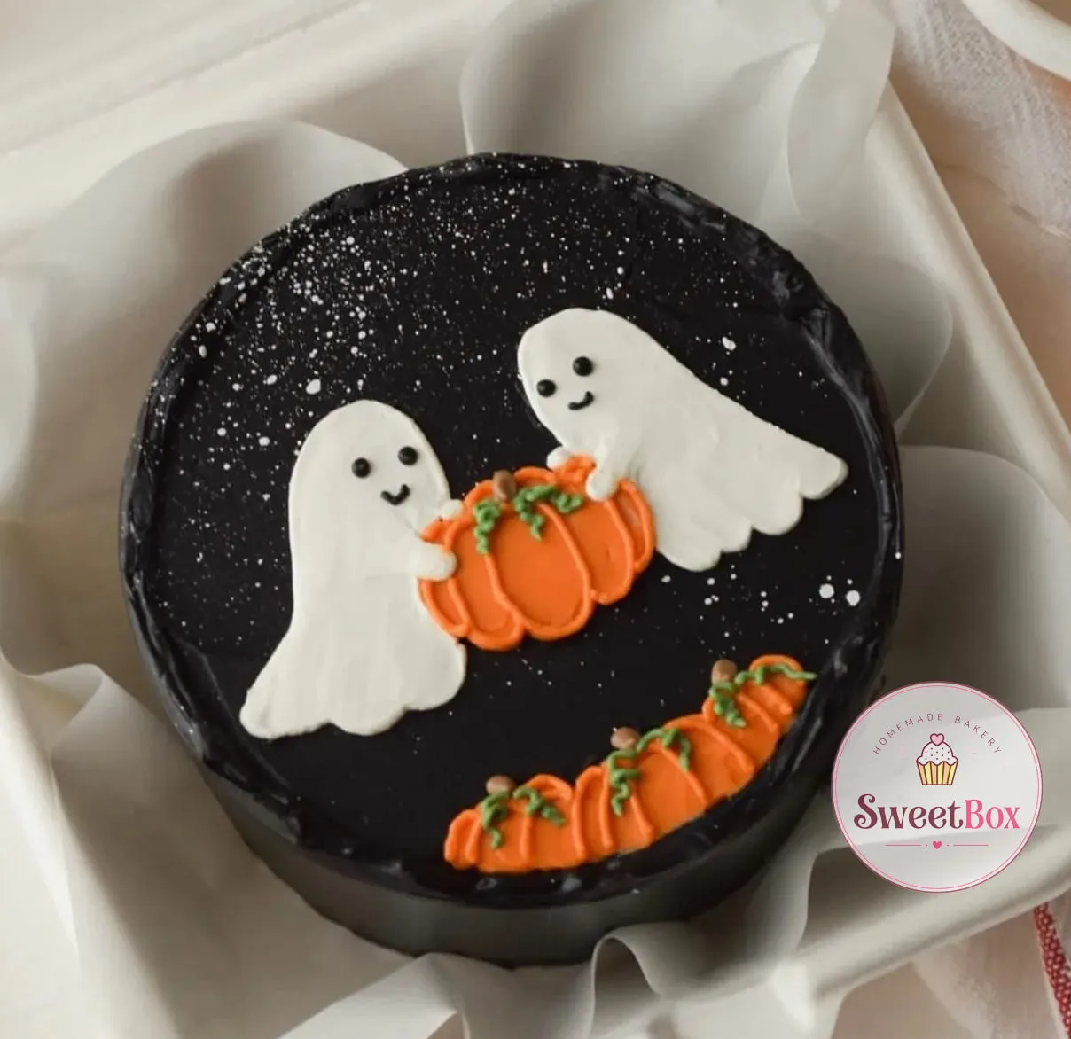 Black bento cake in a box with two smiling white ghosts carrying an orange pumpkin under a starry sky
