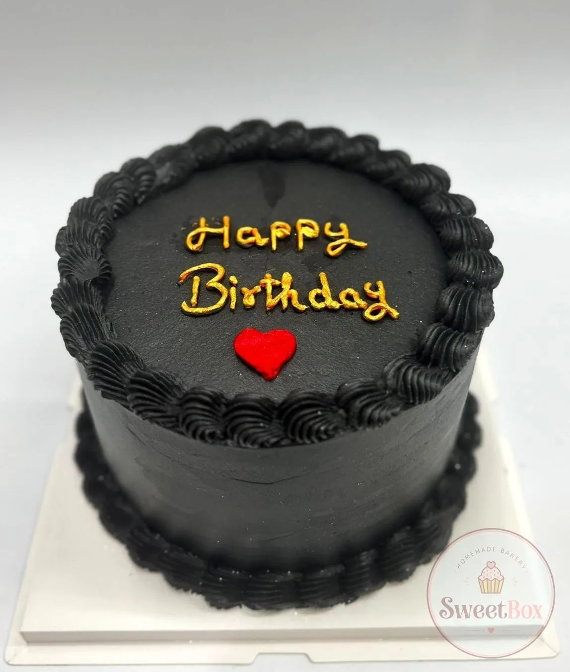 Black cake with piped shell borders, gold Happy Birthday script and a red heart