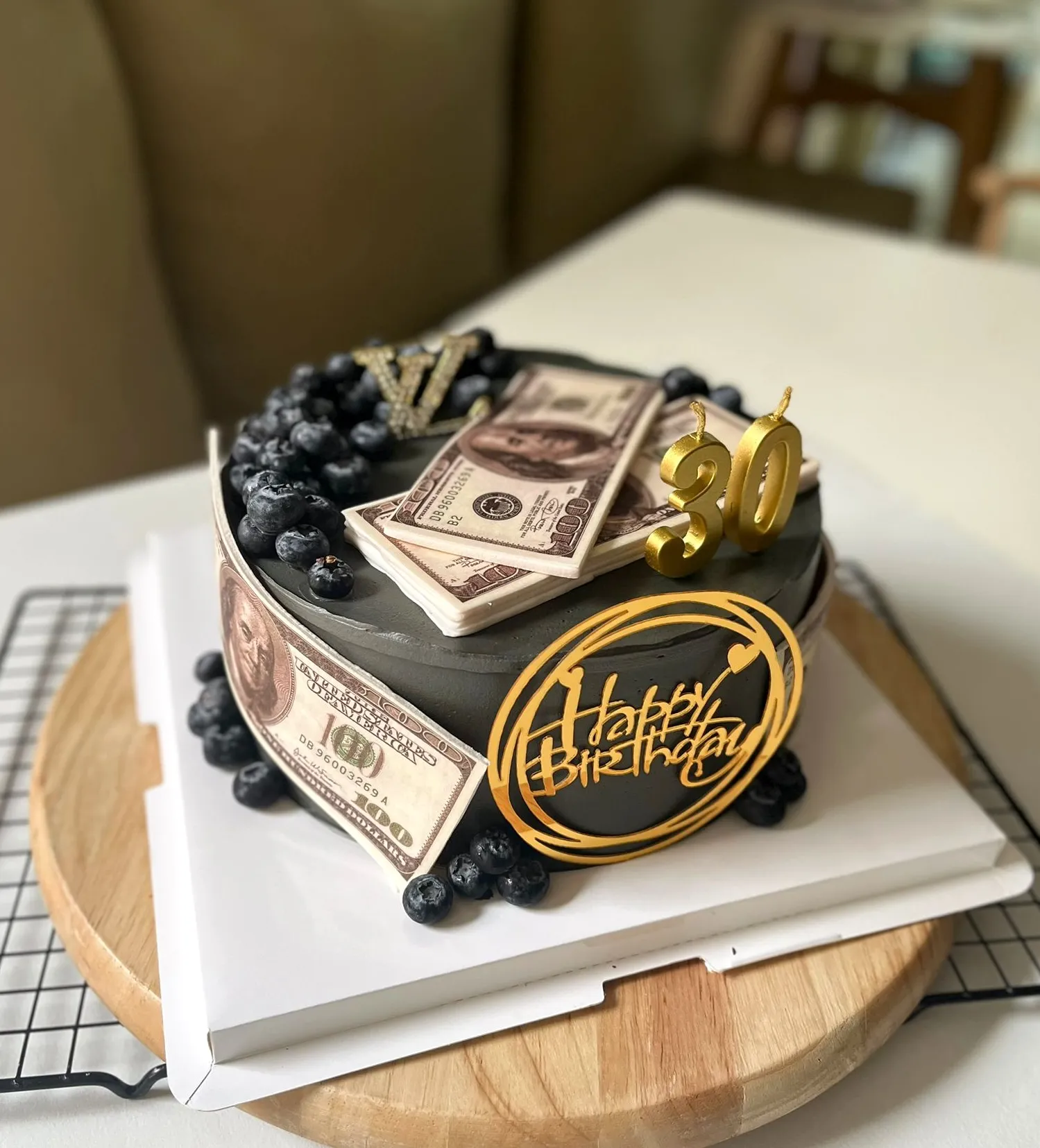 Black 30th birthday cake wrapped in dollar bills with blueberries and gold Happy Birthday toppers