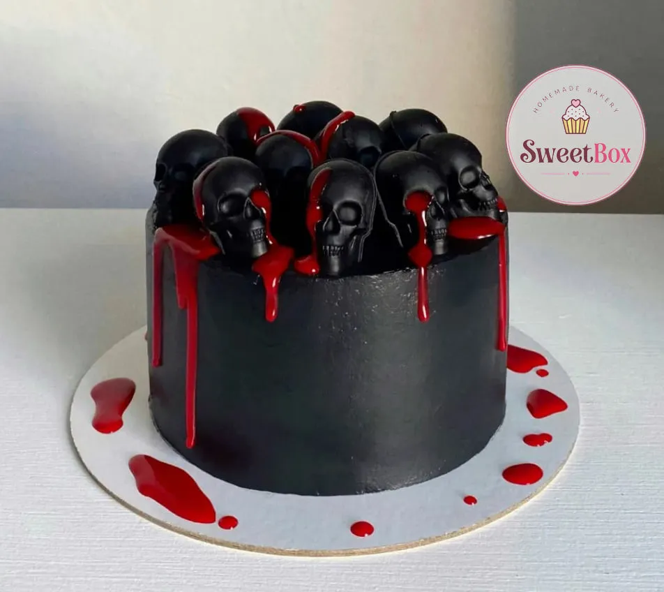 Black cake topped with black chocolate skulls and a red drip running down the side onto the board