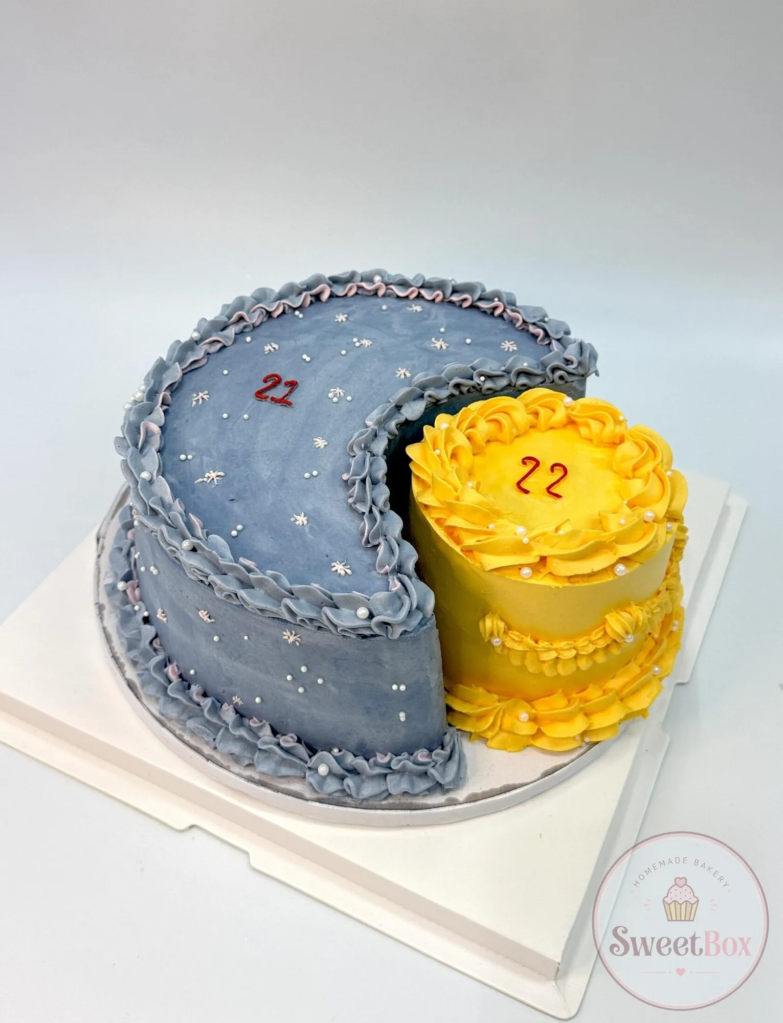 Denim-blue crescent moon cake with piped ruffles and tiny stars, with a small yellow cake set into its curve