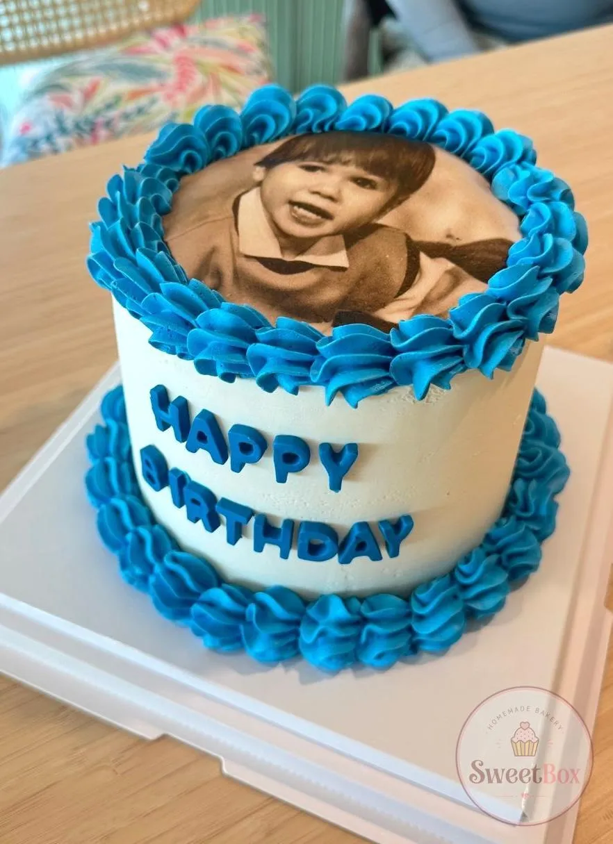 White cake with blue piped borders, a sepia childhood photo on top and Happy Birthday on the side
