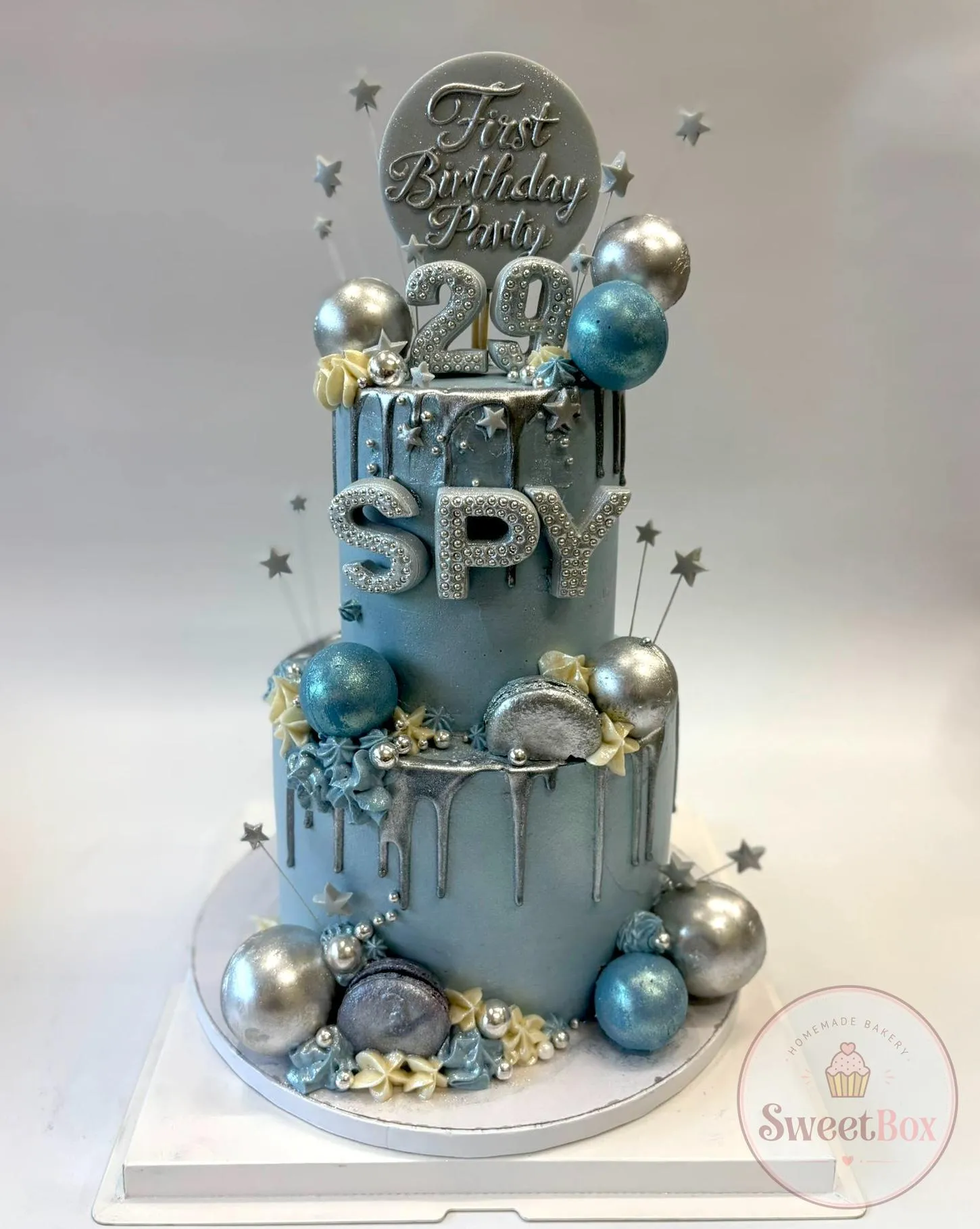 Blue and silver two-tier birthday cake with metallic spheres, silver drip, stars and a number 29