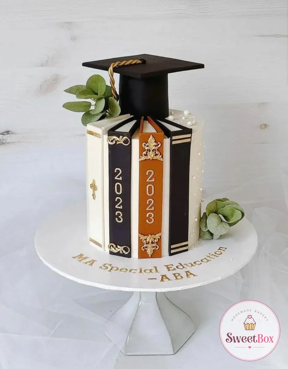 White graduation cake with book spines marked 2023, a black mortarboard, eucalyptus and MA Special Education lettering on the board