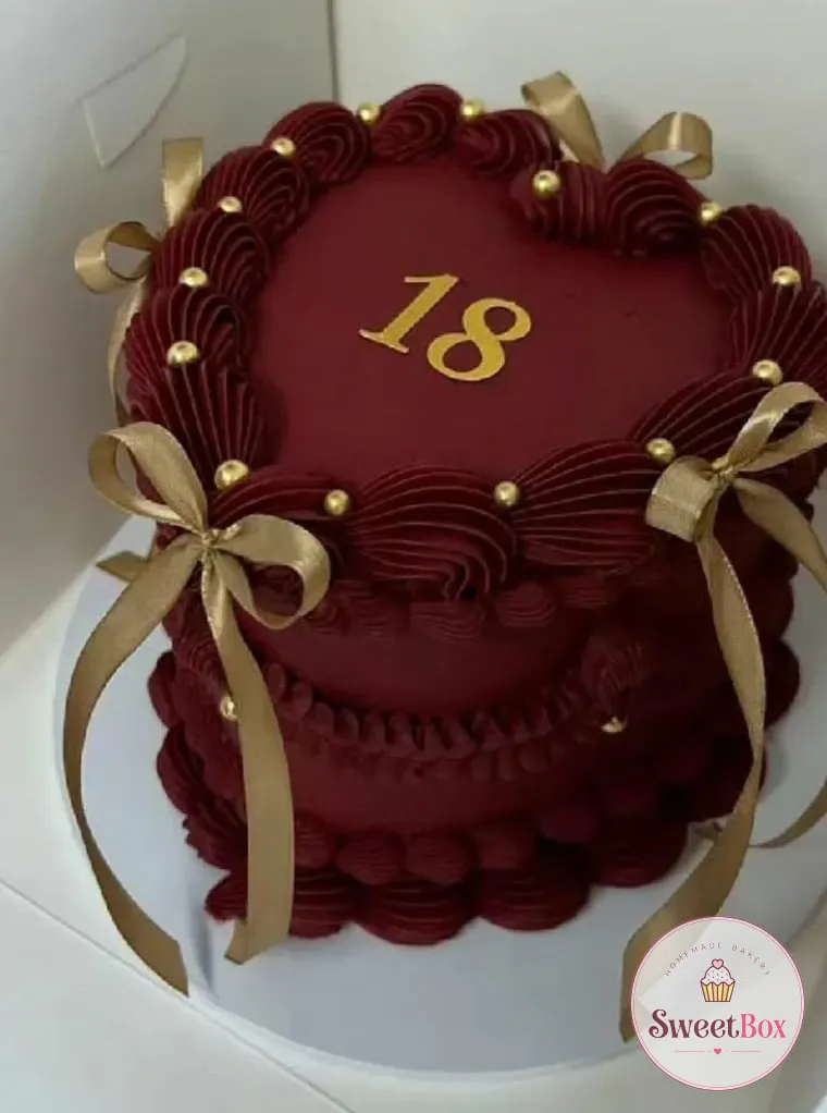Burgundy heart-shaped vintage cake in a box with piped shell borders, gold pearls, gold ribbon bows and a gold number 18
