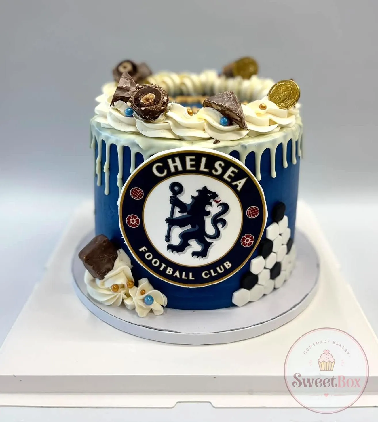 Navy cake with a football club crest, white drip, cream rosettes, chocolates, gold coins and black and white hexagons