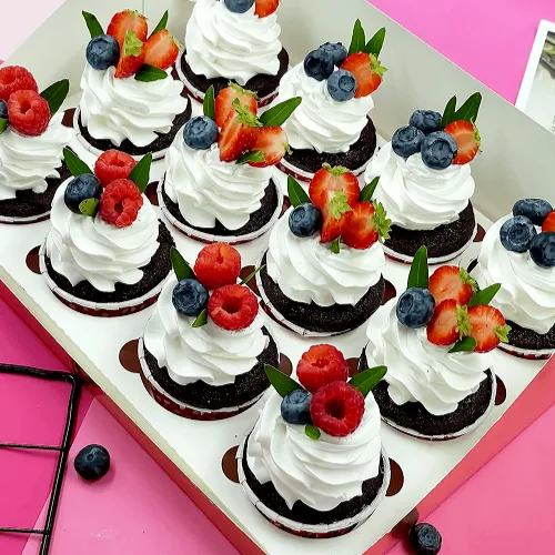 Assorted chocolate cupcakes topped with whipped cream, strawberries, raspberries and blueberries