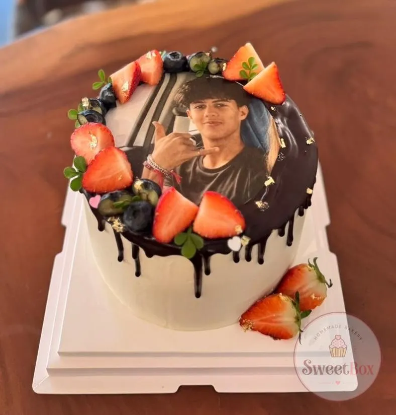 White photo cake with dark chocolate drip, an edible portrait on top and fresh strawberries and blueberries