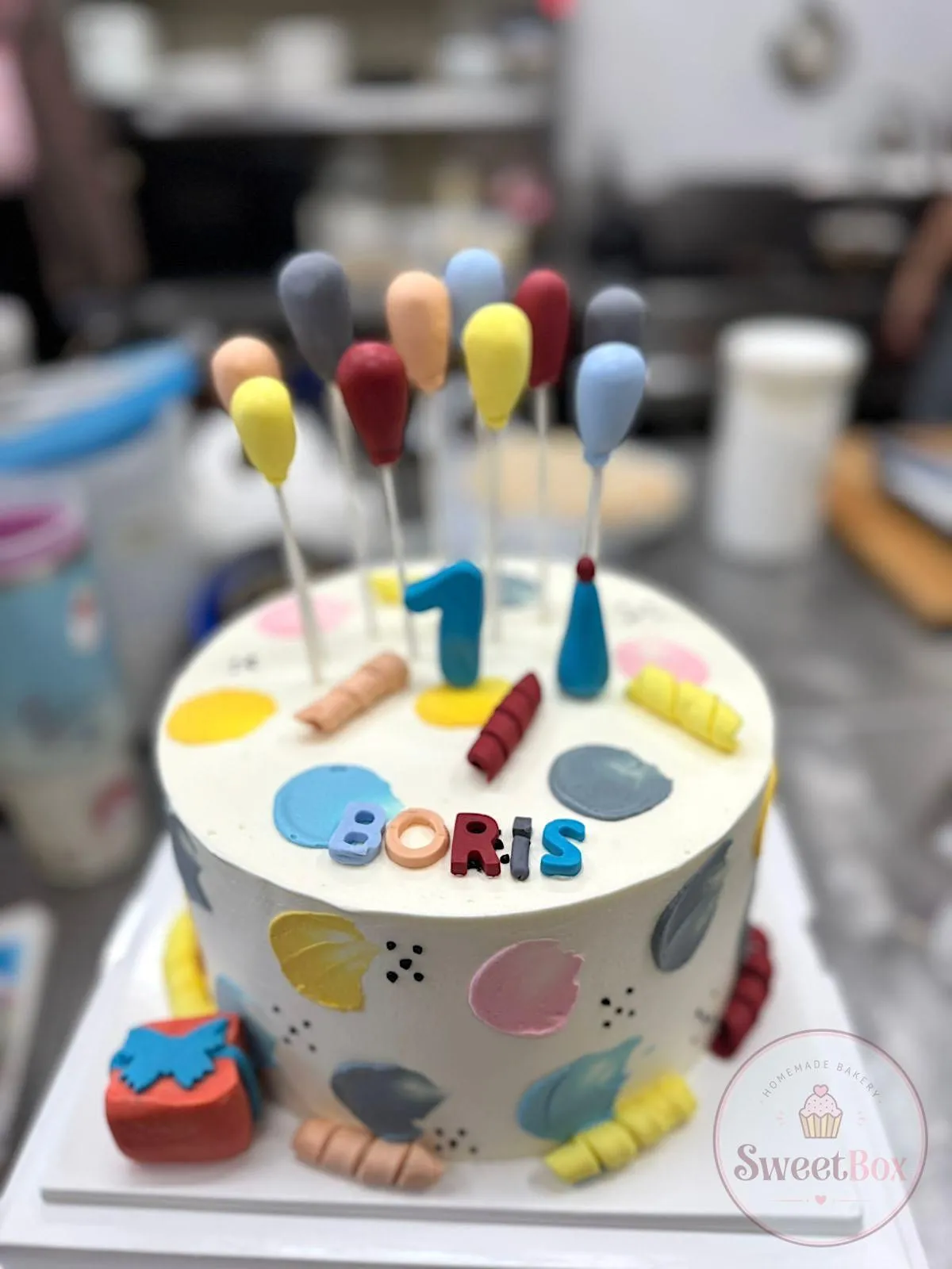 First birthday cake with colorful balloon toppers, a paint-dot design and a personalized name
