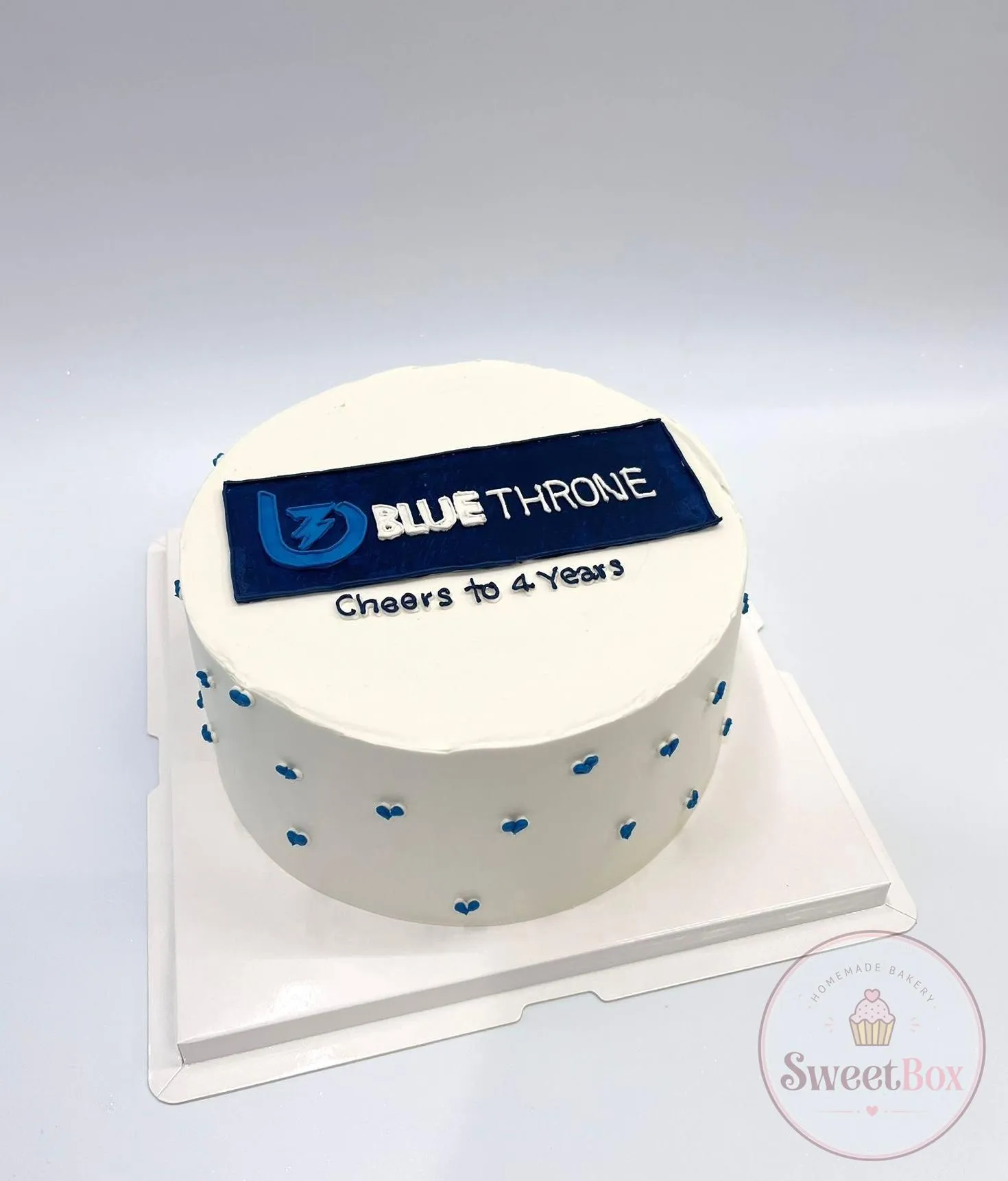 White corporate cake with a printed company logo plaque, blue dots and a Cheers to 4 Years message