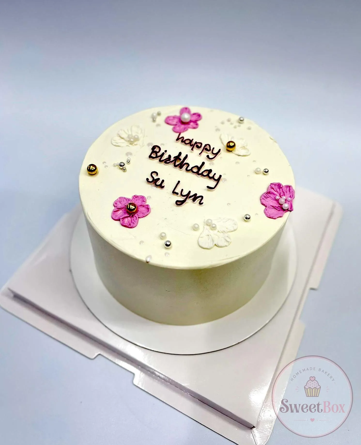 Cream cake with pink sugar flowers, pearls and a handwritten Happy Birthday message with a name