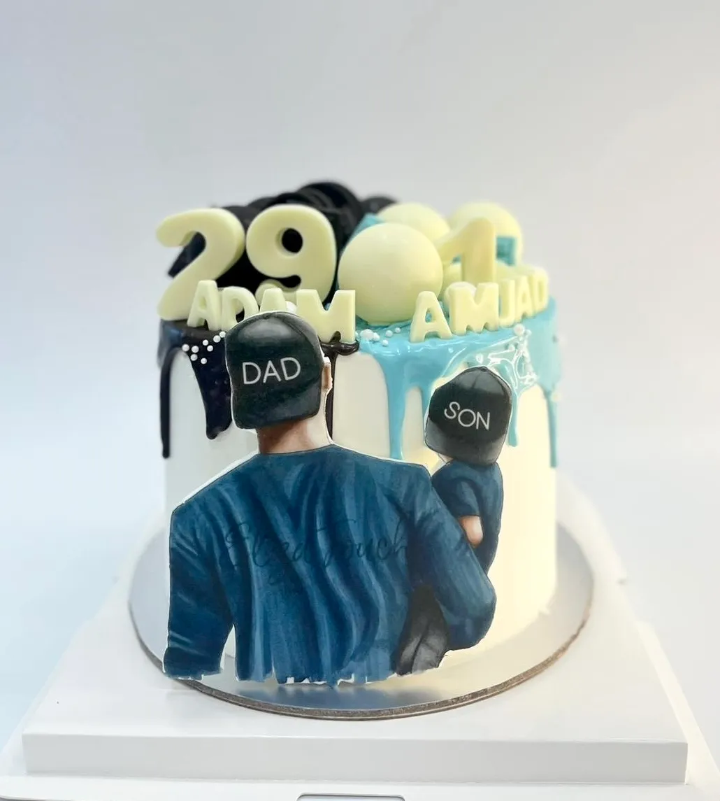 White cake with dark and light blue drip, a printed dad and son picture and numbers 29 and 1 with two names