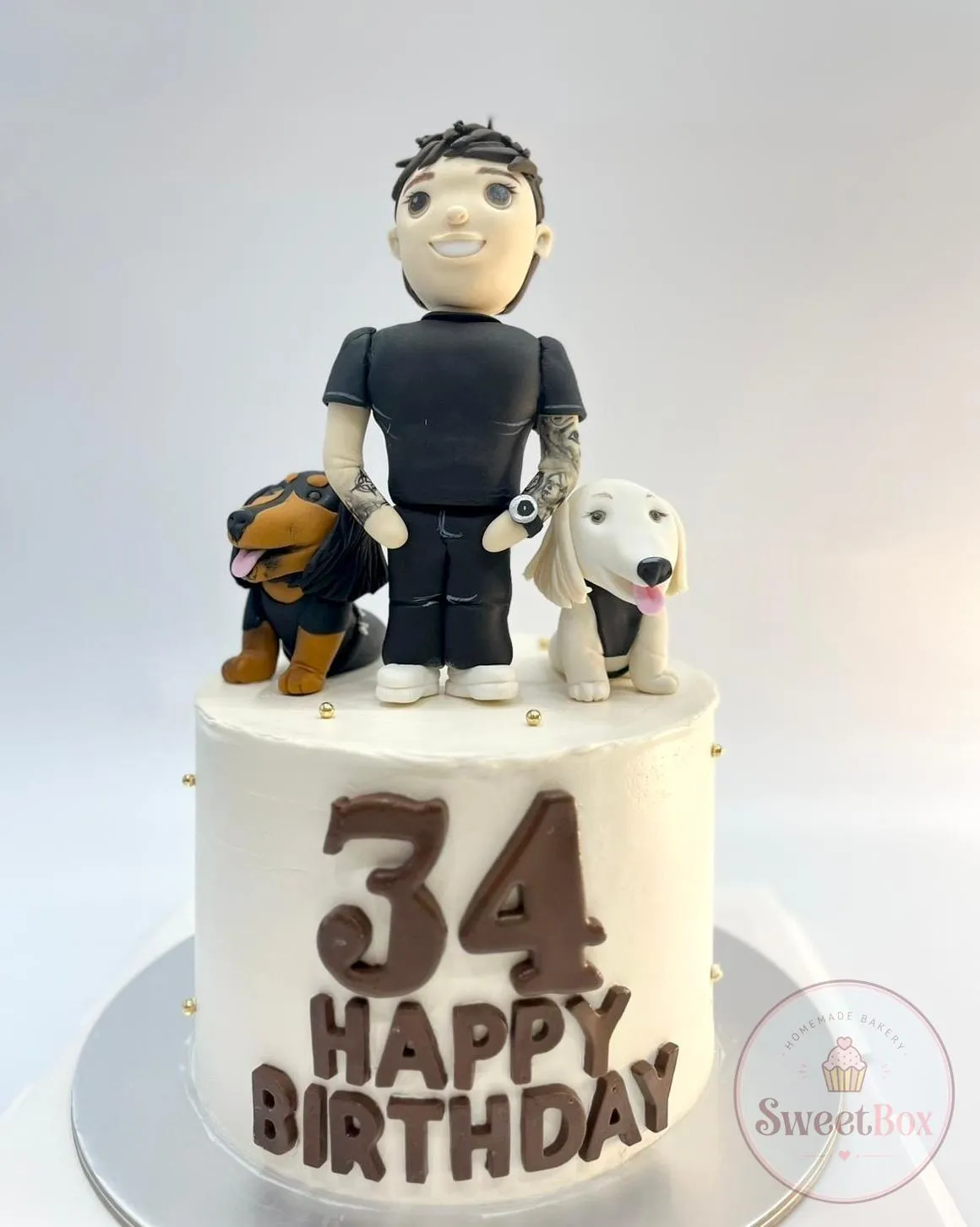 White birthday cake with a fondant man figurine and his two dogs, a chocolate number 34 and Happy Birthday