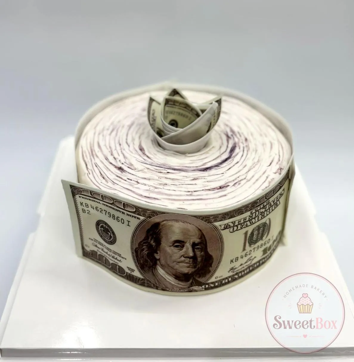 Cake shaped like a tight roll of edible hundred-dollar bills with a folded money crown on top