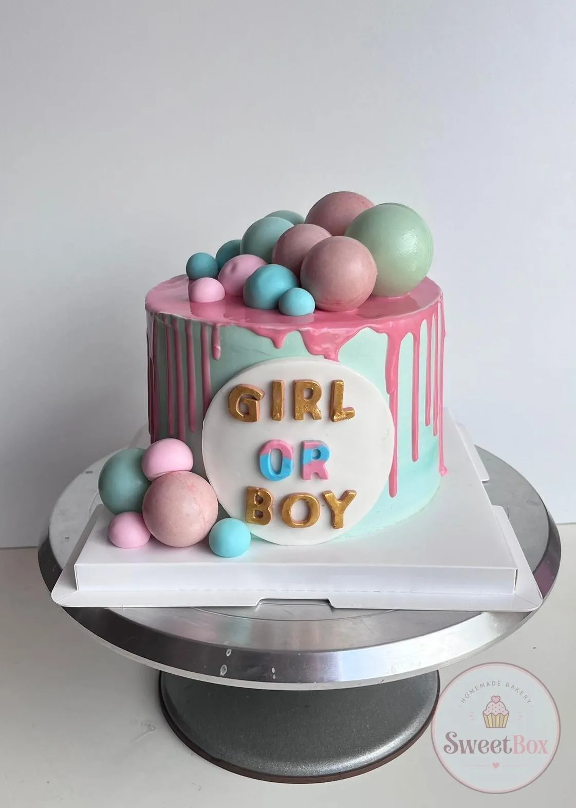 Mint cake with pink drip, pastel pink, blue and green spheres and a Girl or Boy plaque with gold letters