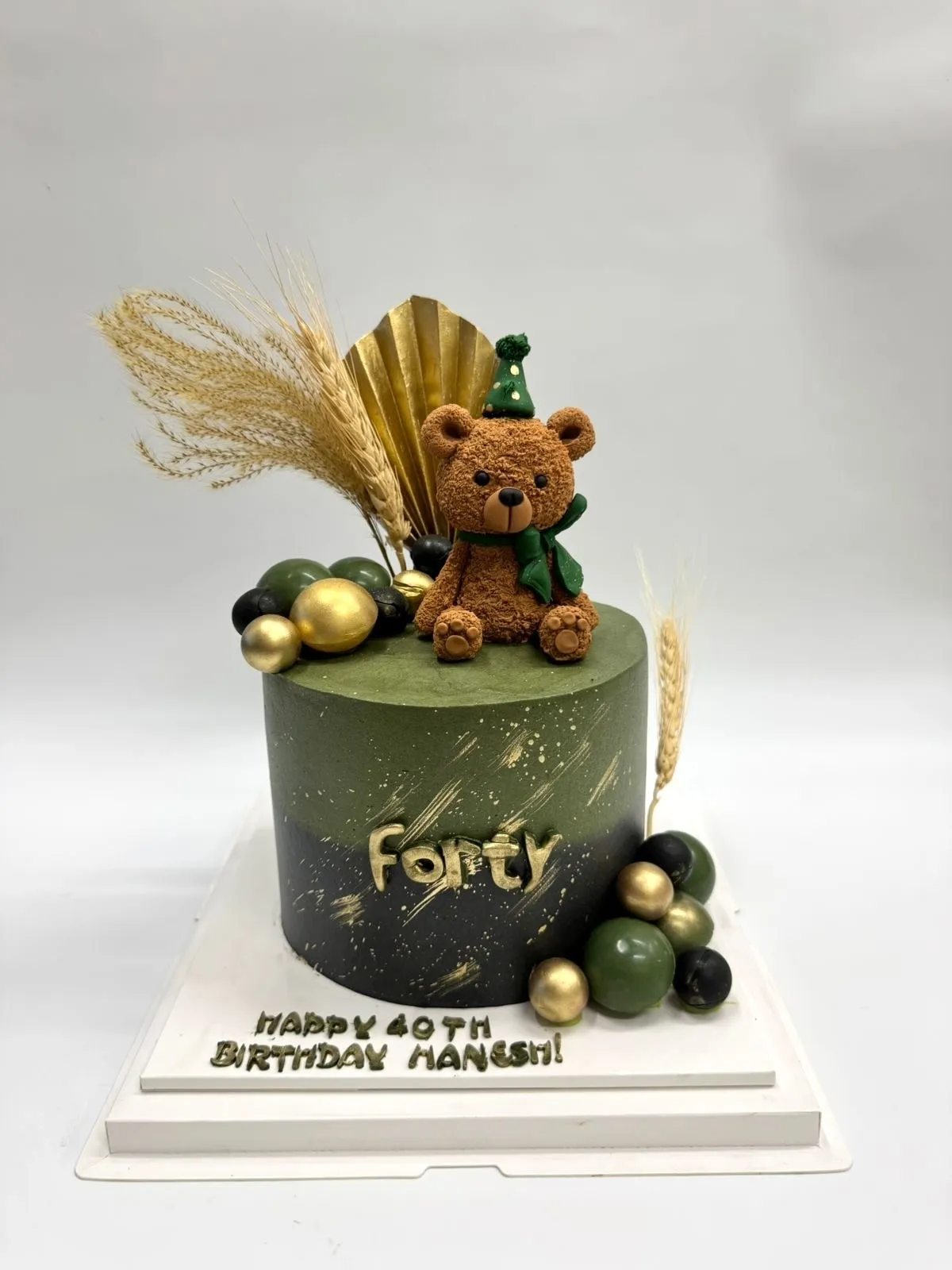 Olive green and black cake with a teddy bear in a party hat, gold Forty lettering and a Happy 40th Birthday message on the board
