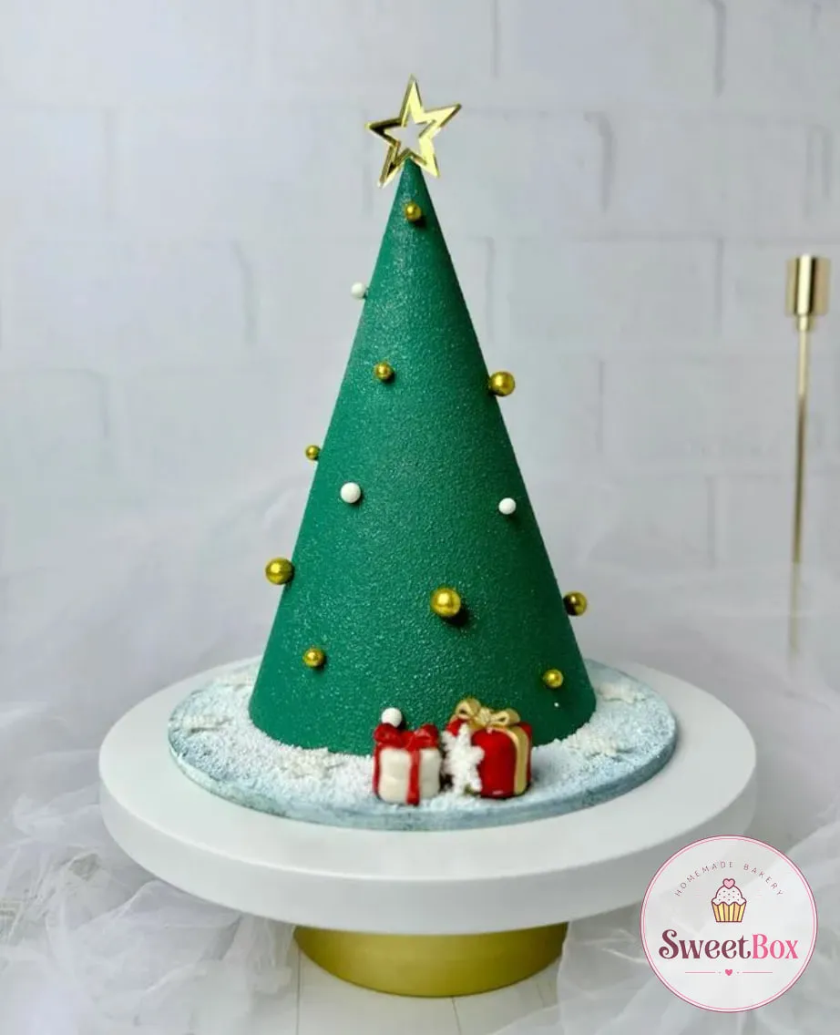Green cone-shaped Christmas tree cake with gold and white pearls, a gold star topper and two tiny red gift boxes on a snowy board
