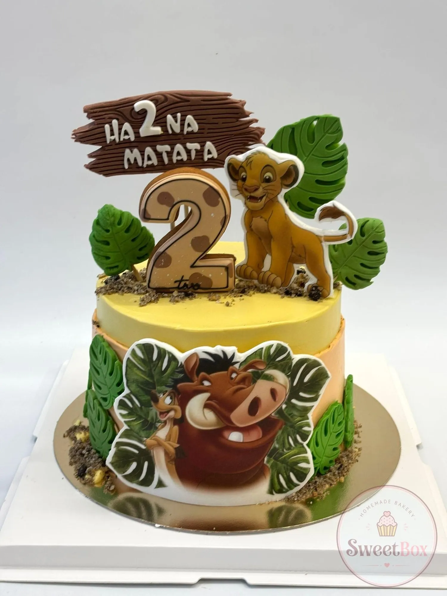 Yellow second birthday cake with Simba, Pumbaa, palm leaves and a wooden Hakuna Matata sign