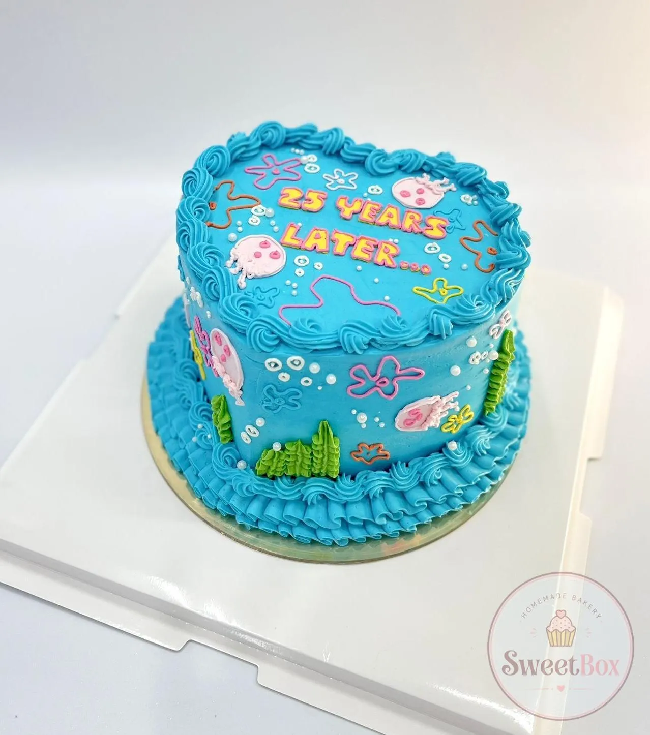 Blue heart-shaped cake with 25 years later lettering, jellyfish and seaweed doodles in an underwater style