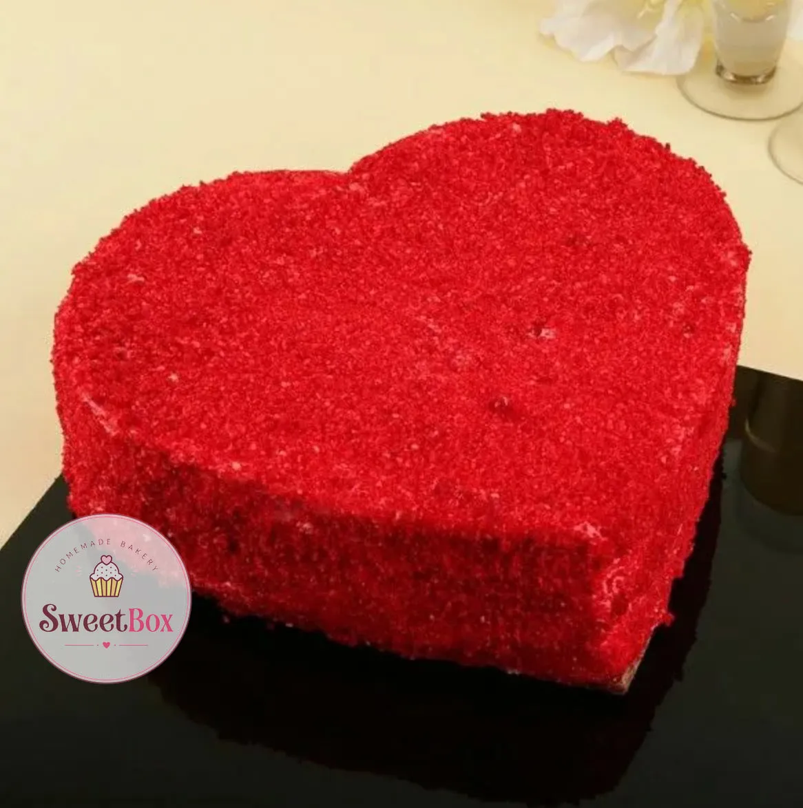 Heart-shaped red velvet cake covered in red velvet crumbs on a black board