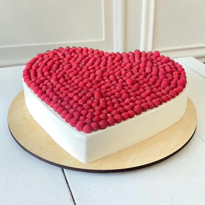 Heart-shaped white cream cake covered with fresh raspberries on a wooden board