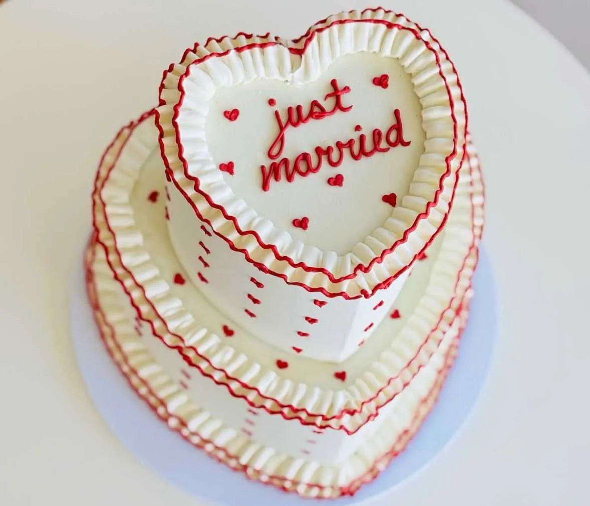 Two-tier heart-shaped Just Married cake with white and red vintage piping and small red hearts