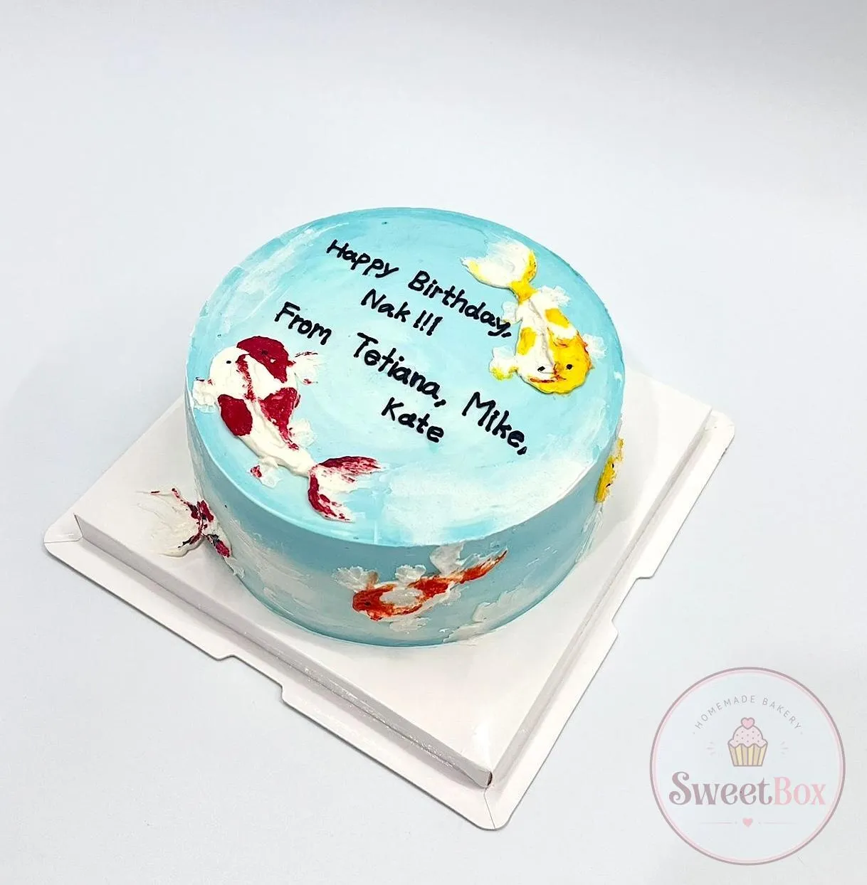 Pale blue watercolor cake with painted koi fish and a handwritten birthday message