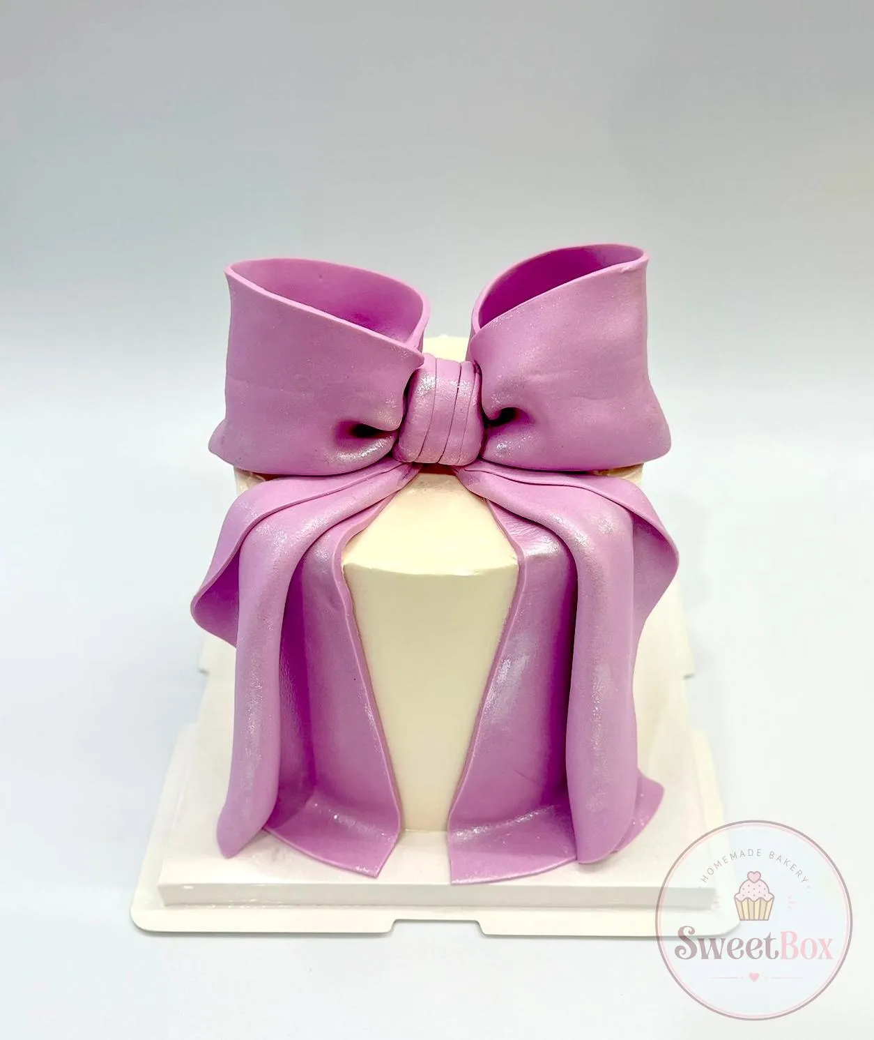 Tall white cake wrapped like a gift with a big shimmering lilac fondant bow and long draped ribbons