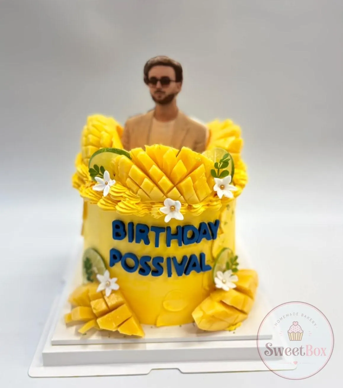 Yellow cake with fresh mango, lime slices and white flowers, a photo cutout of a man and Birthday Possival lettering