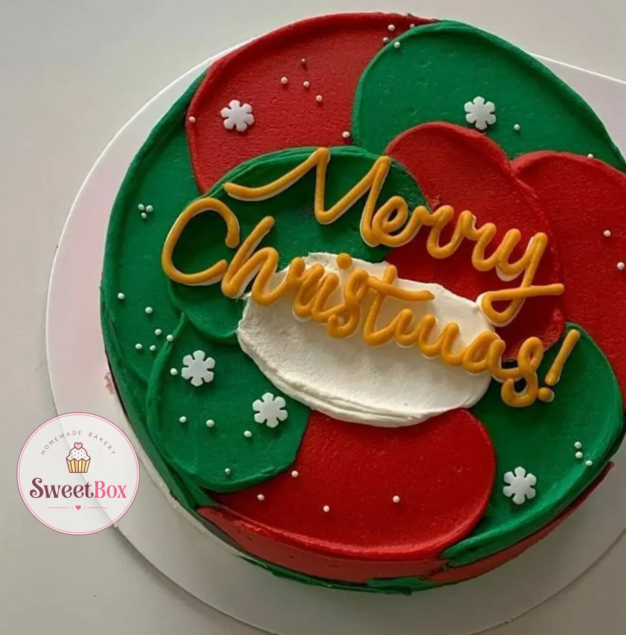Round cake with red and green cream swirls, white sugar snowflakes and gold Merry Christmas! script