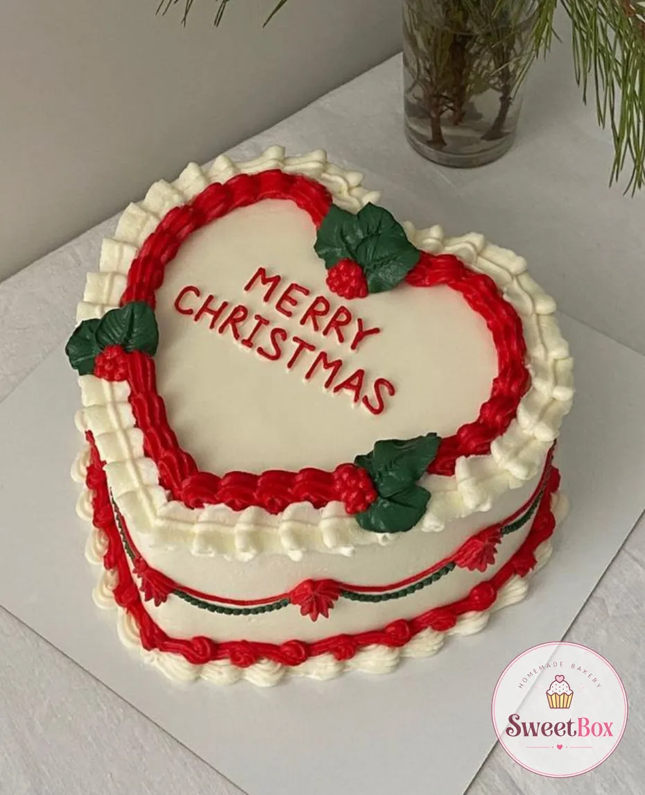 White heart-shaped cake with red piped borders, holly leaves with berries and red Merry Christmas lettering