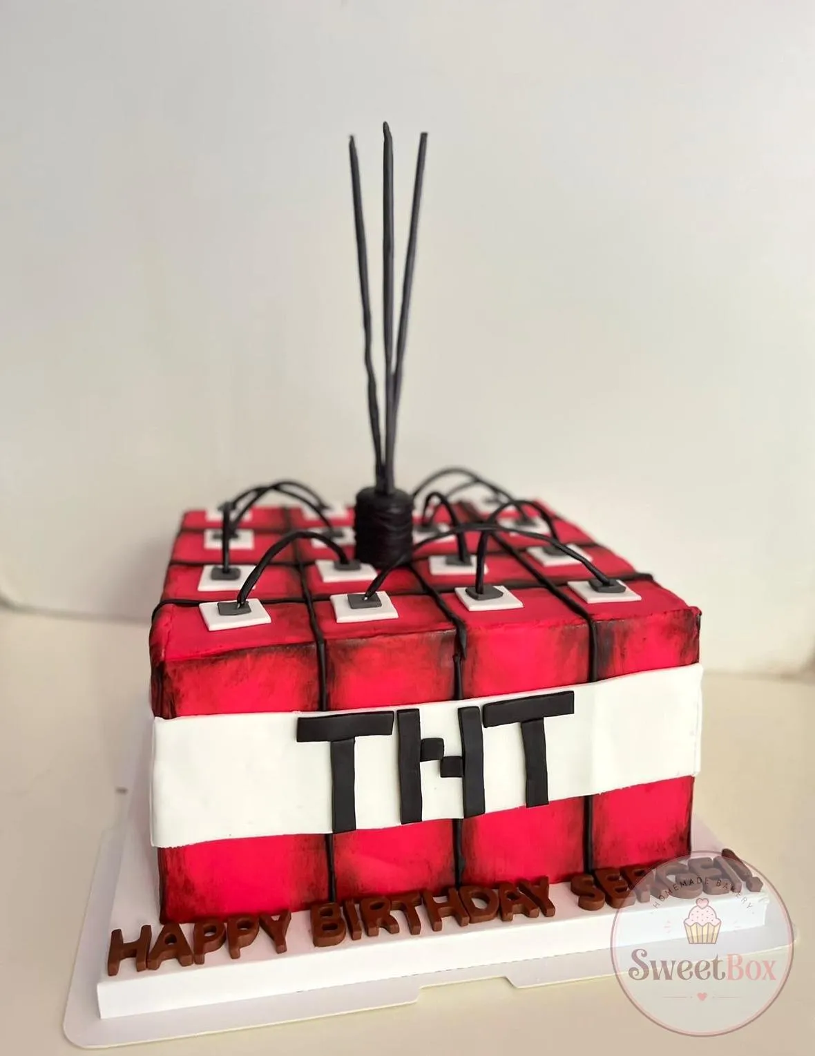 Square red and white TNT block cake inspired by Minecraft with black fuses on top and Happy Birthday letters on the board