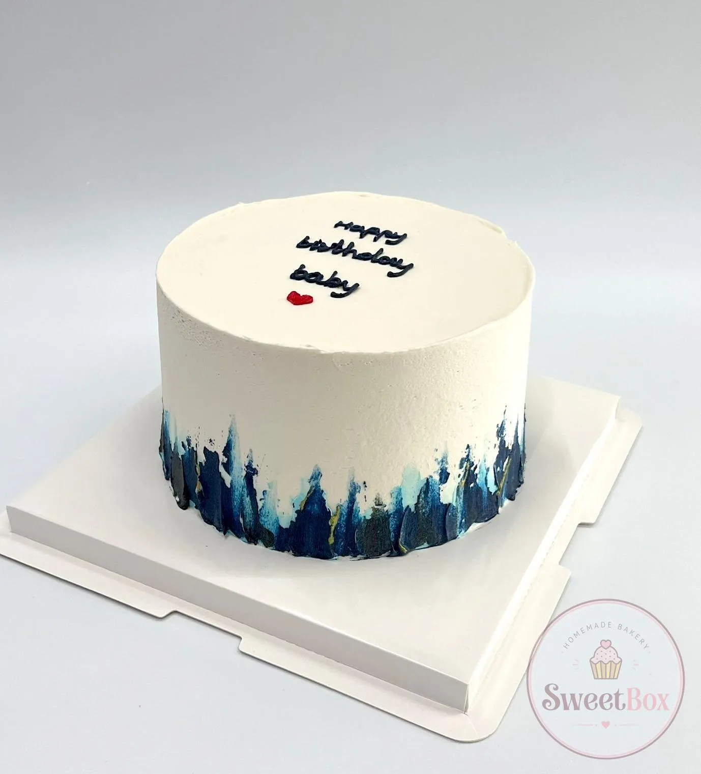 Minimalist white cake with a navy brushstroke base and a handwritten happy birthday baby message