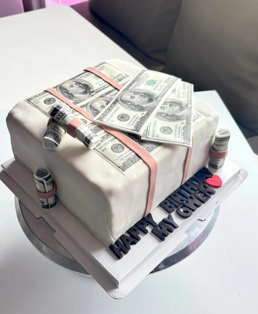 Money stack birthday cake covered in edible dollar bills with a Happy Birthday plaque