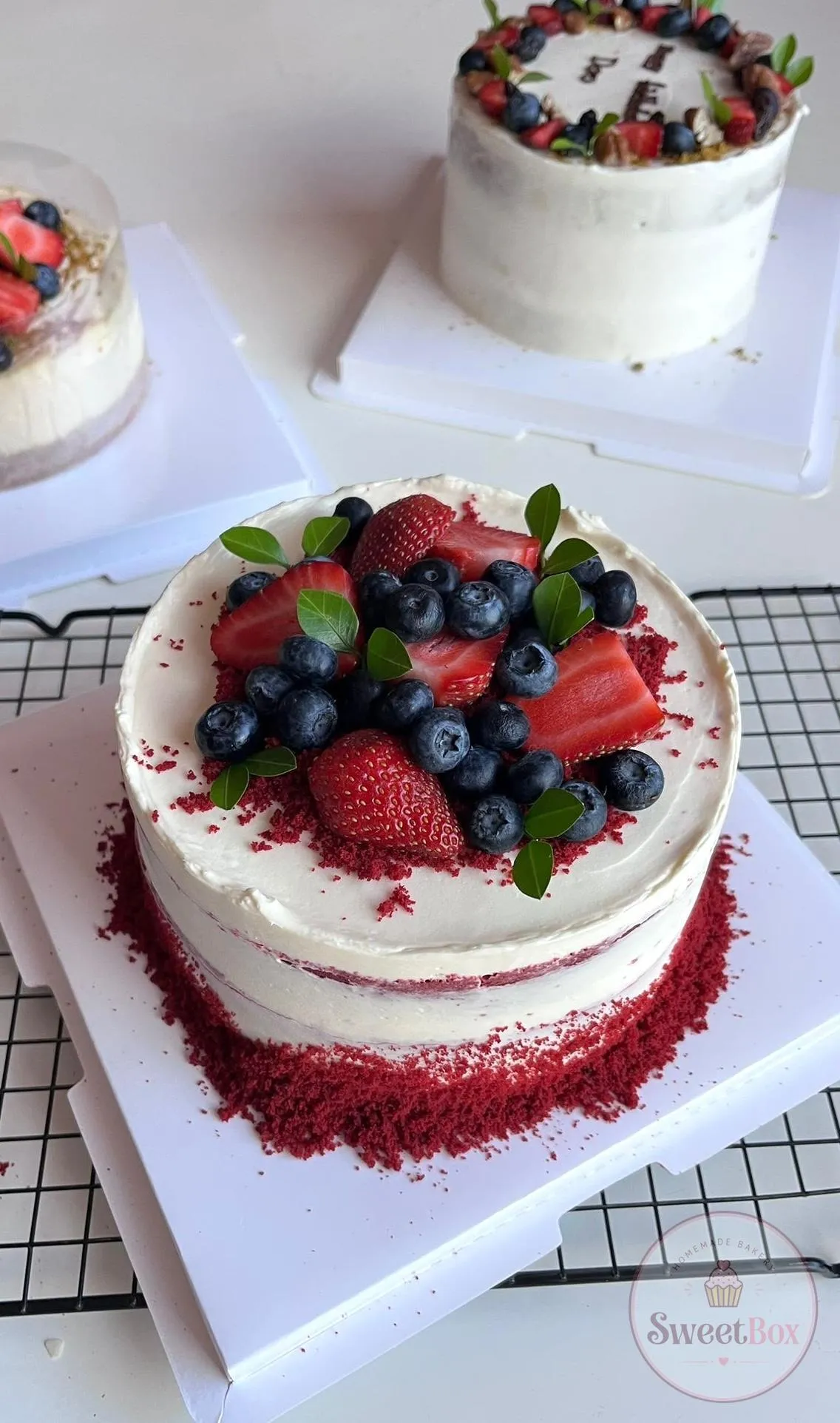 Semi-naked red velvet cake with red crumb at the base, topped with strawberries, blueberries and green leaves