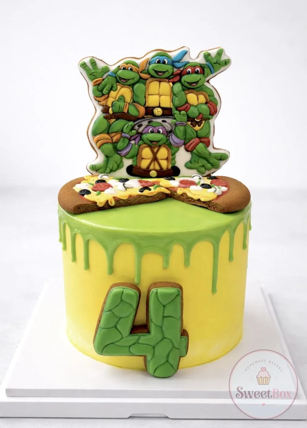 Yellow cake with green drip, a Ninja Turtles cookie topper, pizza cookies and a green number 4