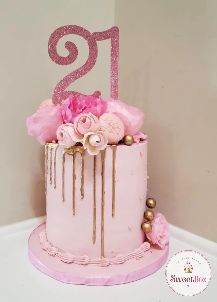 Tall pale pink cake with a gold drip, pink flowers, gold spheres and a pink glitter number 21 topper