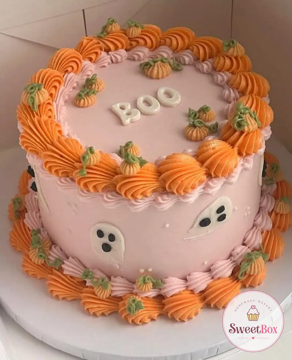 Pastel pink vintage cake with orange piped shells, tiny cream pumpkins, white ghosts on the side and BOO letters on top
