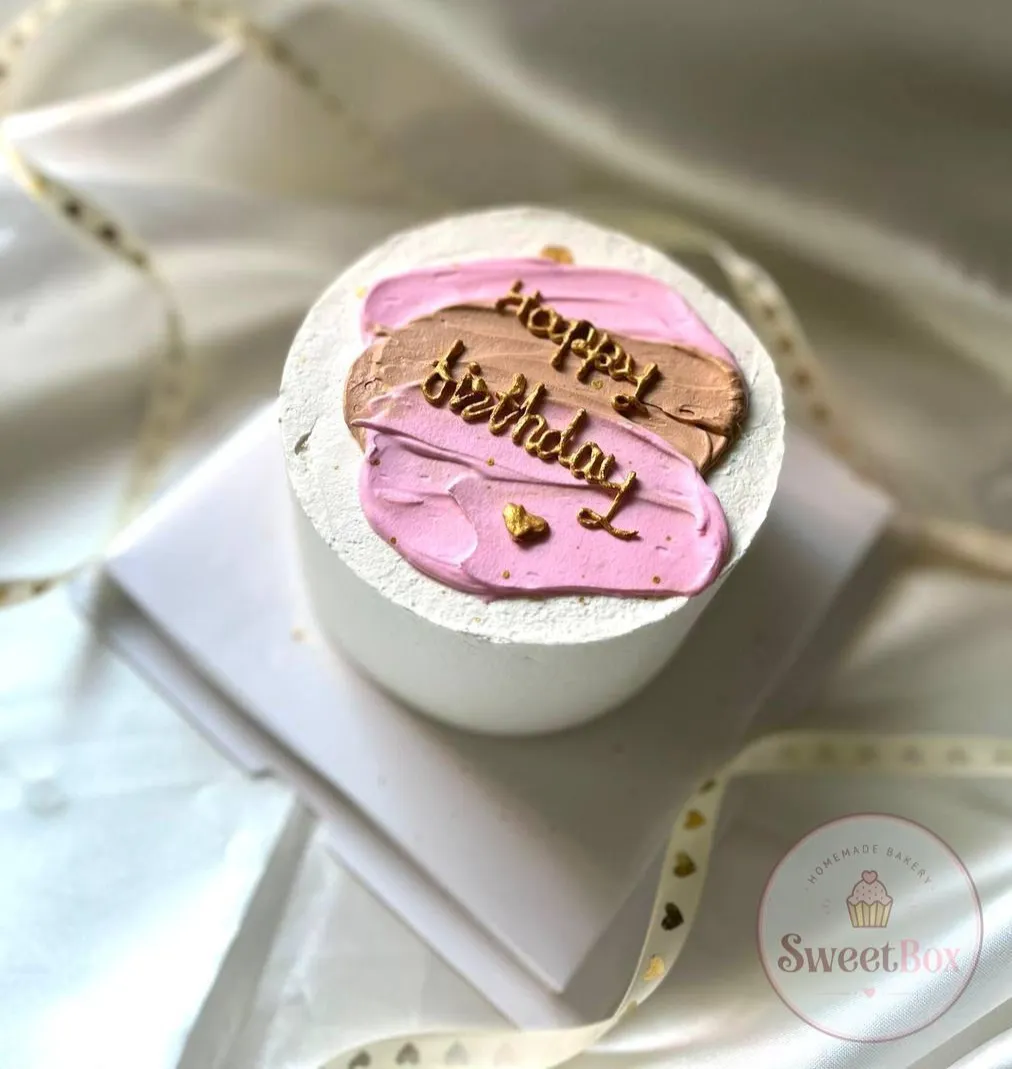 Small white bento cake with pink and brown brushstrokes and gold Happy Birthday script