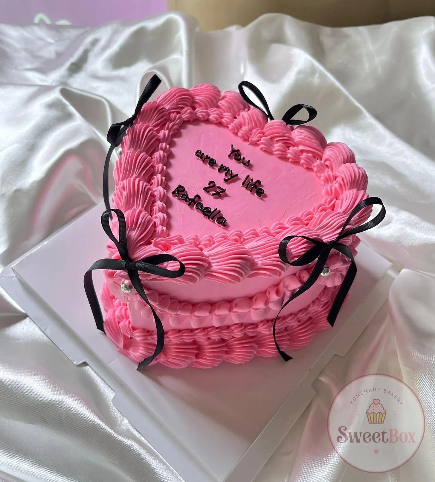 Hot pink heart-shaped vintage cake with piped shells, black ribbon bows and a You are my life message