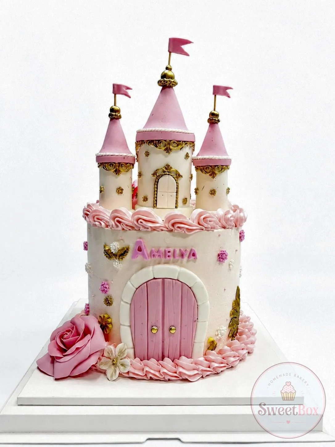 Pink and white princess castle cake with turrets, pink flags, gold details, a pink rose and a name