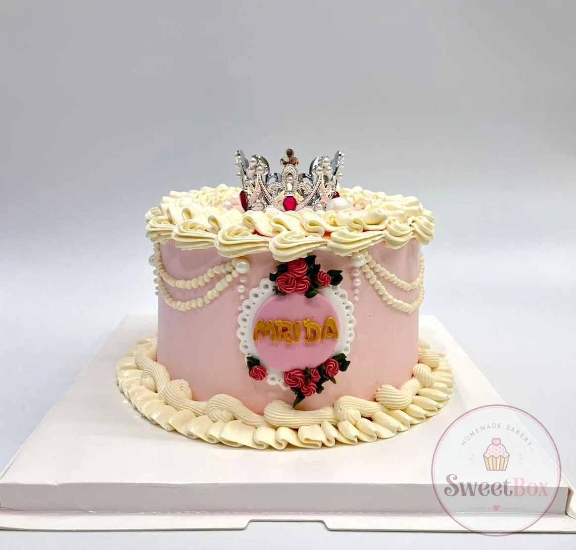 Pink vintage cake with cream piping, pearl swags, piped red roses, a silver crown and a name plaque