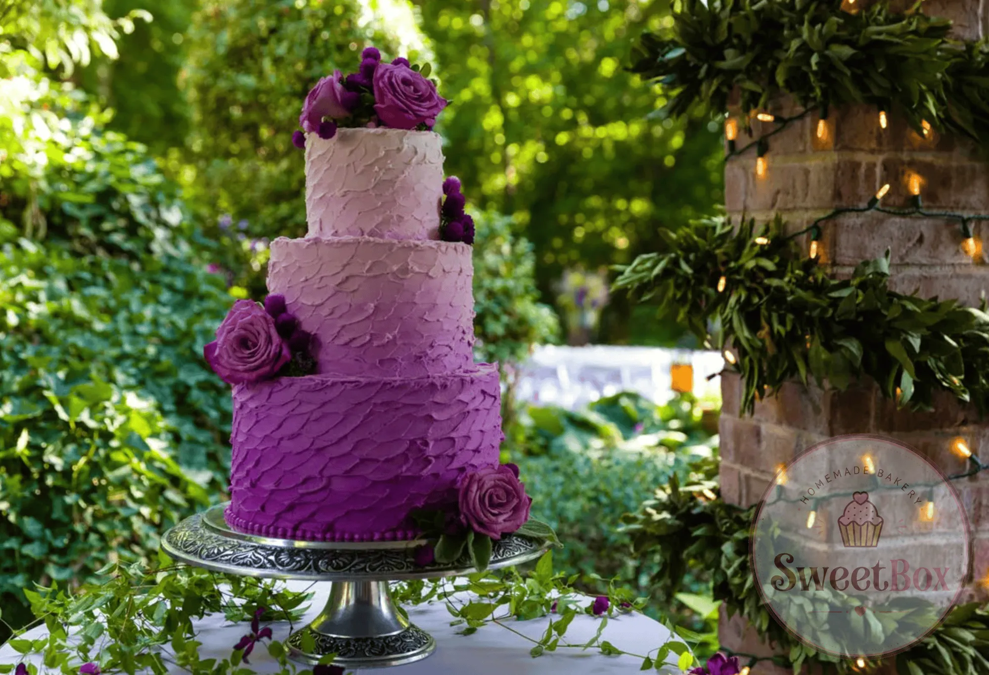 Three-tier purple ombre cake with violet roses on a stand in a lush garden setting