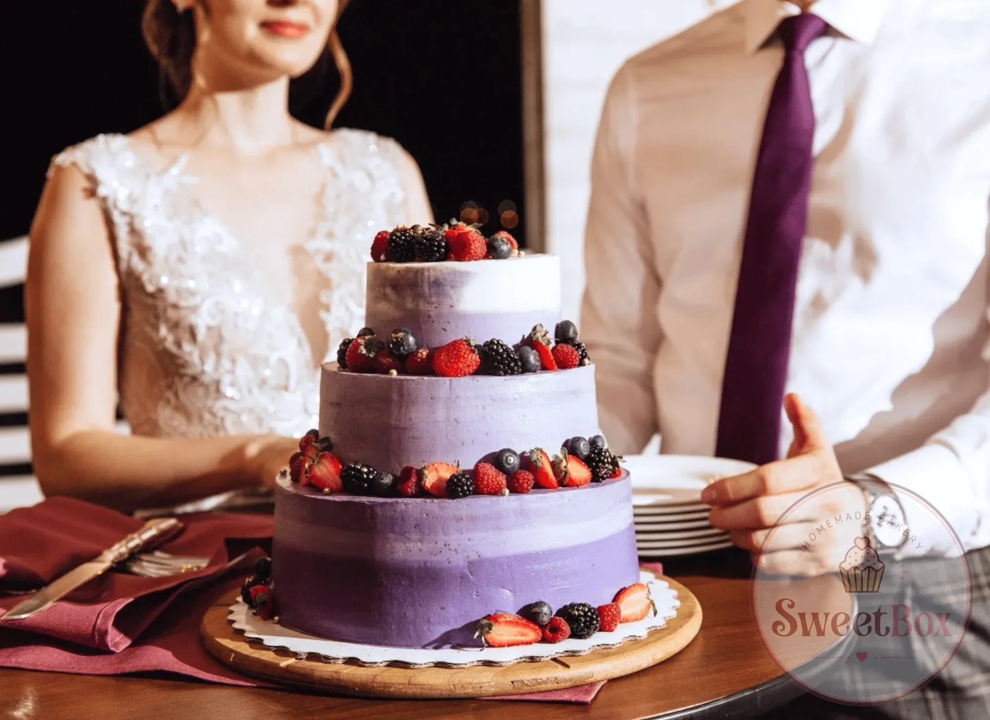 Three-tier purple ombre wedding cake with fresh berries on a table in front of a bride and groom