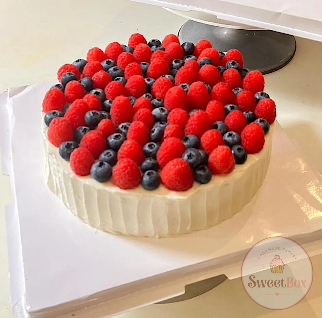 Cream cake generously topped with fresh raspberries and blueberries